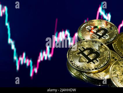 Goldene Bitcoin-Reflexionen isoliert auf dem Spiegel mit einem digitalen Börsenchart. Krypto-Währung BTC Golden Bitcoin selektiver Fokus Nahaufnahme. Stockfoto