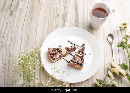 Auf dem Teller sind zwei Scheiben Käsekuchen mit Tee und Blumen, mit Platz für Glückwünsche Stockfoto