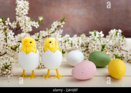 Spielzeug Küken, die aus Eiern schlüpfen, bunte Ostereier und Pflaumenblumen auf einem Holztisch. Osterkonzept. Stockfoto