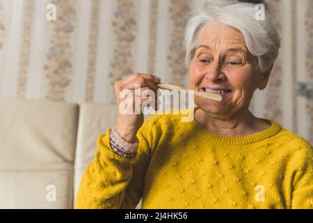 Ältere, kurzhaarige Dame aus Europa, die eine ökologische Bambuszahnbürste in der Hand hält und ihre Zähne putzt. Die Bedeutung der Hygiene. . Hochwertige Fotos Stockfoto