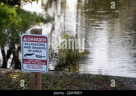 Ein Schild an einem Fluss in Orlando, Florida, USA, warnt vor Alligatoren und Schlangen in der Gegend. Stockfoto