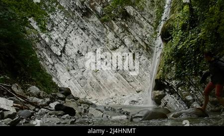 Berge überwuchert mit Gras, auf dem der Wasserfall fließt. Kreativ. Menschen zu Fuß in der Nähe von schönen Landschaften und Bergen, durch die Bäche und Stockfoto