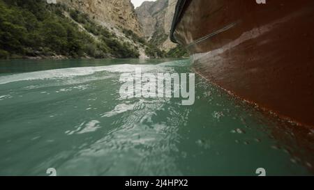 Das Meer, das sich unter dem Boot entwickelt. Aktion. Leuchtend blaues Wasser unter dem Boot auf dem Hintergrund der schönen grünen Sommerberge. Stockfoto