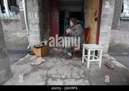 Mariupol. 14. April 2022. Eine Frau sitzt in der Nähe eines beschädigten Gebäudes in Mariupol, 14. April 2022. Kredit: Victor/Xinhua/Alamy Live Nachrichten Stockfoto