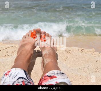 Weibliche Füße mit heller Blume am Sandstrand. Stockfoto