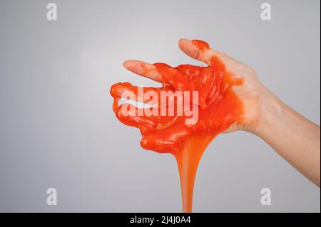 Roter Schleim, der aus der Hand einer Frau auf einem weißen Hintergrund herabfließt. Stockfoto