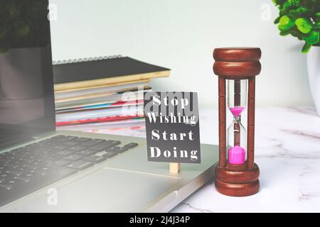 Motivierendes Zitat auf einem Schwarzen Brett auf einem Laptop oder Notebook mit Sanduhr - Stop Wishing Start doing. Stockfoto