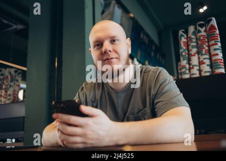 Smartphone-Mann sms-SMS trinken im Café Sommer. Fröhlicher, lässiger, kahlbärtiger Mann in der Stadt Stockfoto