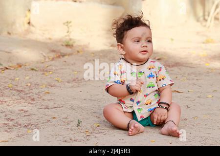 Nahaufnahme eines Portraitfotos eines kleinen neugeborenen niedlichen Hindu-Babys, das draußen mit lächelndem Gesicht auf dem Boden sitzt, Indien Stockfoto
