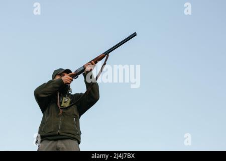 Männlicher Jäger mit Gewehr, der in der Natur auf den Vogel zielt Stockfoto