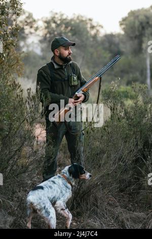 Hunter Mann mit einer Waffe, die draußen mit seinem Hund auf der Suche nach einer Beute steht. Stockfoto
