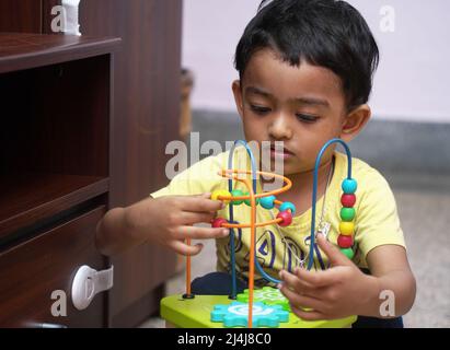 Ein indischer Baby Junge beschäftigt mit einem Perlen Puzzle-Spielzeug, Entwicklungsaktivität Meilenstein Konzept Bild. Stockfoto