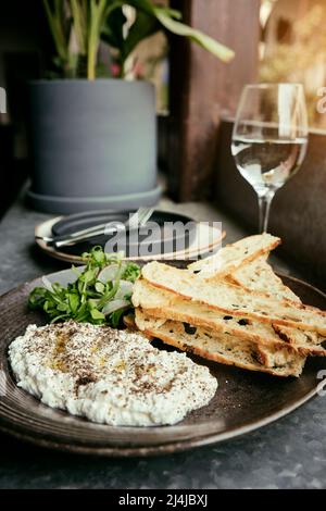 Italienischer Käse stracciatella -Büffelmozzarella- auf einem schwarzen Teller serviert mit frischem Rucola und geröstetem Brot. Präsentation des Küchenchefs. Stockfoto