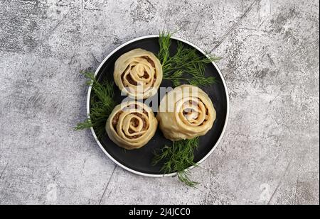 Manti gedämpfte Knödel mit Fleisch und Kartoffeln auf einem runden Teller auf dunkelgrauem Hintergrund. Draufsicht, flach liegend Stockfoto