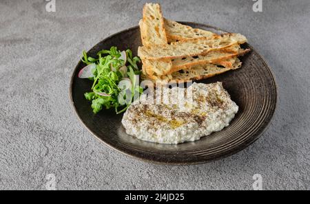 Italienischer Käse stracciatella -Büffelmozzarella- auf einem schwarzen Teller serviert mit frischem Rucola und geröstetem Brot. Präsentation des Küchenchefs. Stockfoto