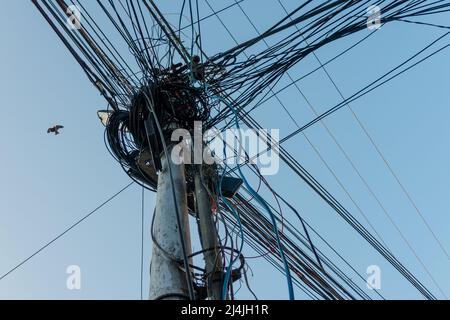 Strommasten mit überfüllten Drähten und Verteilerkästen in Indien. Stockfoto