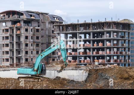 Bagger mit Eimern arbeitet auf der Baustelle vor dem Hintergrund von Häusern im Bau Stockfoto