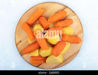 Draufsicht auf gekochte Karotten und Kartoffeln für den Salat auf einem hölzernen Schneidebrett. Nahaufnahme. Stockfoto