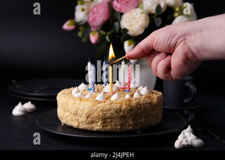 Den ganzen Urlaub Kuchen mit krümeligen Mürbeteig und Mini-Baiser. Mann zündet Kerzen auf einem Kuchen an. Geburtstagskuchen mit brennenden Kerzen. Hausgemachtes Backen. Bl Stockfoto