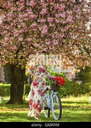 Sakura-Saison. Romantische Fahrradtour. Tourismuskonzept. Transport und Reisen. Mädchen langes Kleid Retro Cruiser Fahrrad Sakura Baum. Frühlingsferien Stockfoto