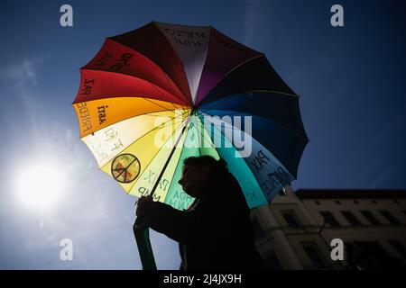 16. April 2022, Berlin: Eine Frau trägt während des ostermarsches des Netzwerks Friedenskooperative einen Regenbogenschirm mit dem Wort 'Frieden' in mehreren Sprachen unter dem Motto 'Lay down your Arms!' In Kreuzberg. Foto: Christoph Soeder/dpa Stockfoto