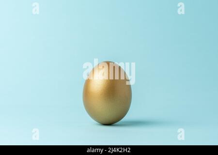 Goldenes Osterei auf blauem Hintergrund. Minimales Osterkonzept. Kreatives Happy Easter oder Frühlingslayout. Stockfoto