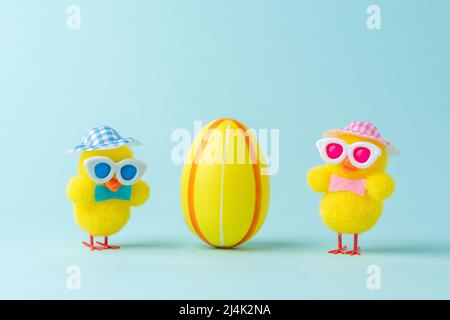 Zwei Hühner mit buntem osterei auf blauem Hintergrund. Minimales Osterkonzept. Kreatives Happy Easter oder Frühlingslayout. Stockfoto