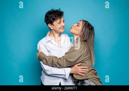 Schöne Familie von Mutter und Tochter zusammen, umarmt und küsst auf blauem Studiohintergrund Stockfoto
