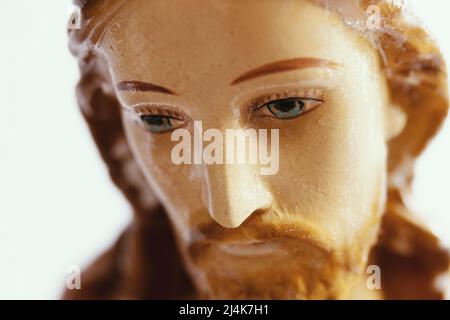 Gesicht von Jesus, der aus der Nähe nach unten schaut. Porträt einer kleinen Jesus Christus Statue oder Figur aus Porzellan oder Ton mit gemalten Elementen. Stockfoto