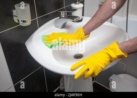 Hände in Schutzhandschuhe Reinigung Waschbecken und Wasserhahn mit Mikrofasertuch und Reinigungsmittel, Konzept der Ordnung und Sauberkeit und Hygiene Stockfoto