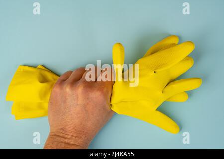 Eine Hand hält zwei gelbe Reinigungshandschuhe aus Gummi Stockfoto