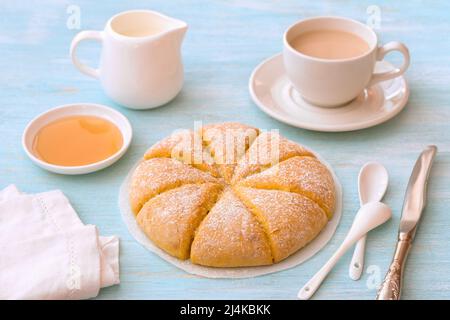 Frisch gebackene Karotten-Scones mit Rahm, Honig und einer Tasse Tee mit Milch auf hellblauem Hintergrund. Leckere hausgemachte Kuchen. Straffung Stockfoto