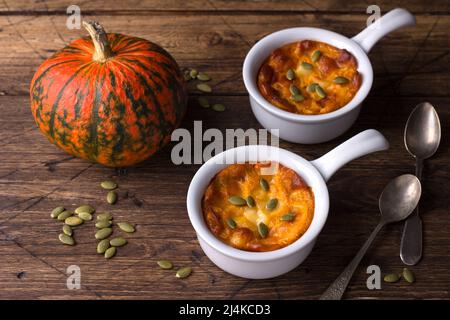 Kürbiskäse-Auflauf in Keramikform mit Kürbiskernen und frischem Kürbis über Holzstruktur-Hintergrund, Freiraum, horizontal Stockfoto