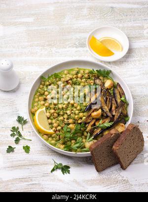 Geschmorte Kichererbsen in grüner Sauce mit gebackener Aubergine, Petersilie und Zitrone auf weißem Holzhintergrund, rustikaler Stil, Draufsicht. Leckeres gesundes Zuhause Stockfoto