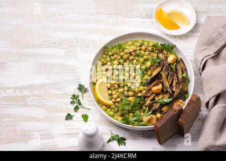 Grüne Kichererbsen mit gebackener Aubergine, Petersilie und Zitrone auf hellem Holztisch, rustikaler Stil, Draufsicht, Freiraum. Leckere gesunde hausgemachte Speisen Stockfoto