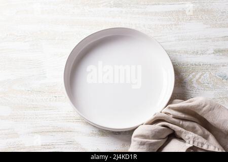 Weißer Teller mit Leinenserviette auf weißem Holzhintergrund, Draufsicht, horizontal Stockfoto