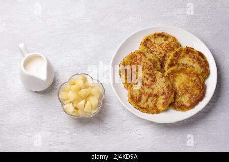 Traditionelle Latkes-Krapfen mit saurer Creme- und Apfelsauce auf hellgrauem texturiertem Hintergrund, Draufsicht Stockfoto