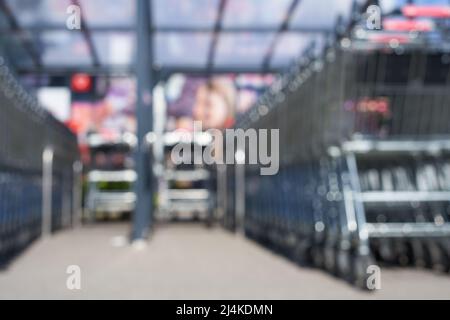 Verschwommen. 2 Reihen mit Warenkörben eines deutschen Lebensmittellauers (kaufland). Plakatwand mit Mädchenkopf. Tiefe Perspektive. Alles außer Fokus. Stockfoto