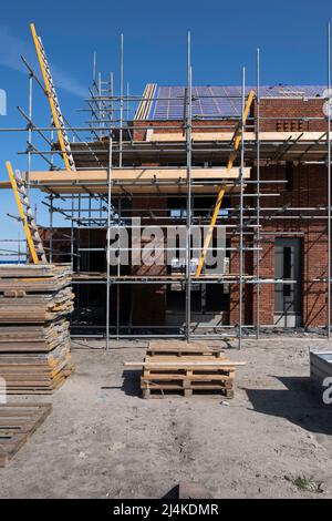 Gerüstbau Pfahlplattform gegen eine neu gebaute Häuserzeile auf einer Baustelle. Es gibt Leitern, um von einer Plattform zur anderen zu klettern Stockfoto