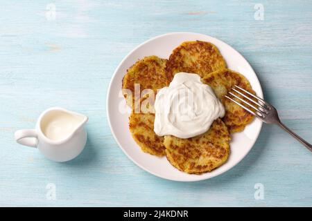 Traditionelle Latkes-Krabben mit saurer Creme auf hellblauem texturiertem Hintergrund, Draufsicht Stockfoto