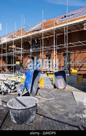 Gerüste auf einer Baustelle einer Reihe neuer Häuser, die gebaut werden sollen. Im Vordergrund Schubkarren und eine Mörserwanne aus Kunststoff Stockfoto