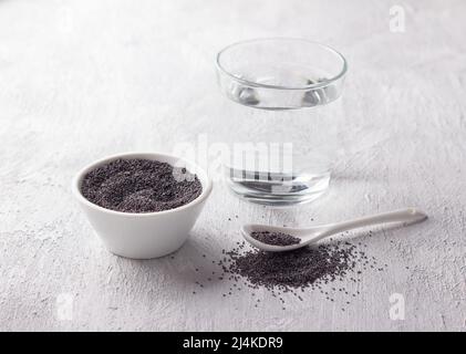 Zutaten für Mohnmilch. mohnsamen in Schüssel und Glas Wasser auf hellgrauem Hintergrund Stockfoto