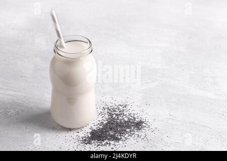 Frische Mohnmilch in der Flasche mit Samen auf hellem Hintergrund. Gesunde Ernährung, veganes Getränk, alternative Milch. Freiraum Stockfoto