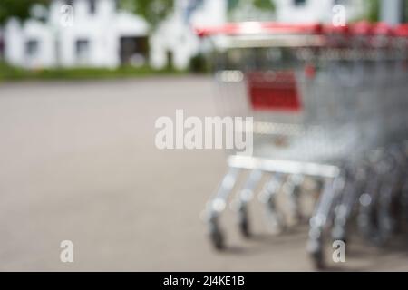 Verschwommen. Einkaufswagen in einer Reihe. Schieben Sie Karren vom Lebensmittelmarkt (Penny) auf einen leeren Parkplatz. Gebäude im Hintergrund. Rückansicht. Alle von f Stockfoto