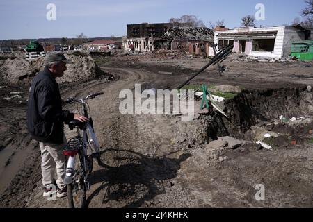 TROSTIANETS, UKRAINE - 15. APRIL 2022 - Ein Mann, der an seinem Fahrrad steht, beobachtet die Zerstörung, die durch den Beschuss russischer Truppen verursacht wurde, wie in der zu sehen ist Stockfoto