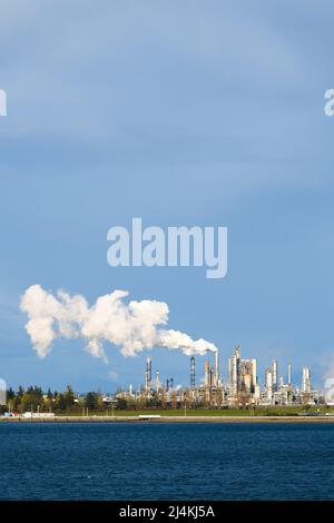 Dampf aus einer Industrieanlage steigt in einen blau bewölkten Himmel. Der Dampf treibt über den Komplex Stockfoto