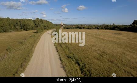 Grünes Feld. Archivmaterial. Riesige Felder mit trockenem Gras neben der Straße, hinter der Sie die Stadt und das Industriegebiet vor dem blauen Himmel sehen können Stockfoto