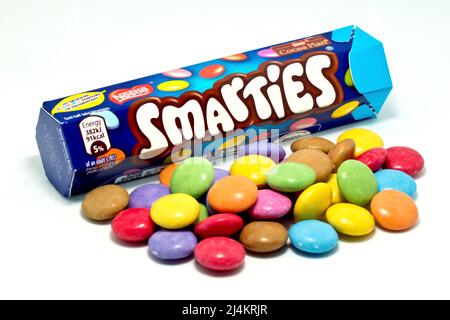 Nahaufnahme eines Tubus von Smarties mit einem Stapel von mehrfarbigen, knusprig geschälten Schokoladenbonbons, isoliert vor weißem Hintergrund. Stockfoto