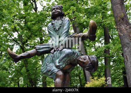 Bronzeskulptur in Form eines spielenden Mädchens, das über einen gekippten Jungen vor dem Hintergrund von Bäumen im Park springt Stockfoto