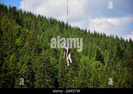 Das Mädchen sprang von der Bungee-Jumping-Fahrt, hängt an einem engen Seil in großer Höhe. Auf einem verschwommenen Hintergrund eines Bergseits Stockfoto